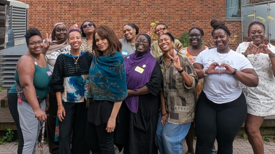 Thirteen women from ADHD Babes stand together outdoors, smiling and making heart shapes with their hands.